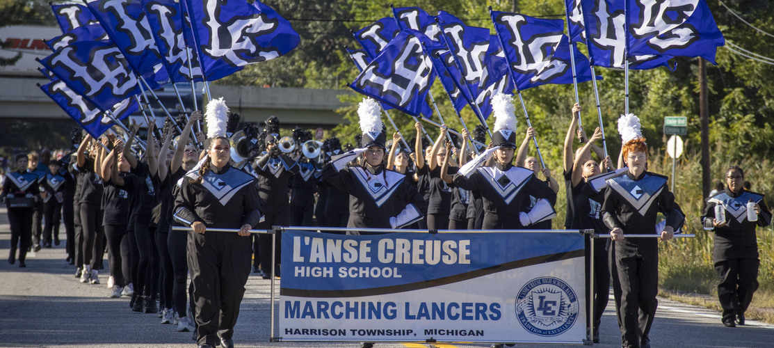 L'Anse Creuse High School Marching Lancers walking down Crocker Boulevard waving flags that say "LC."
